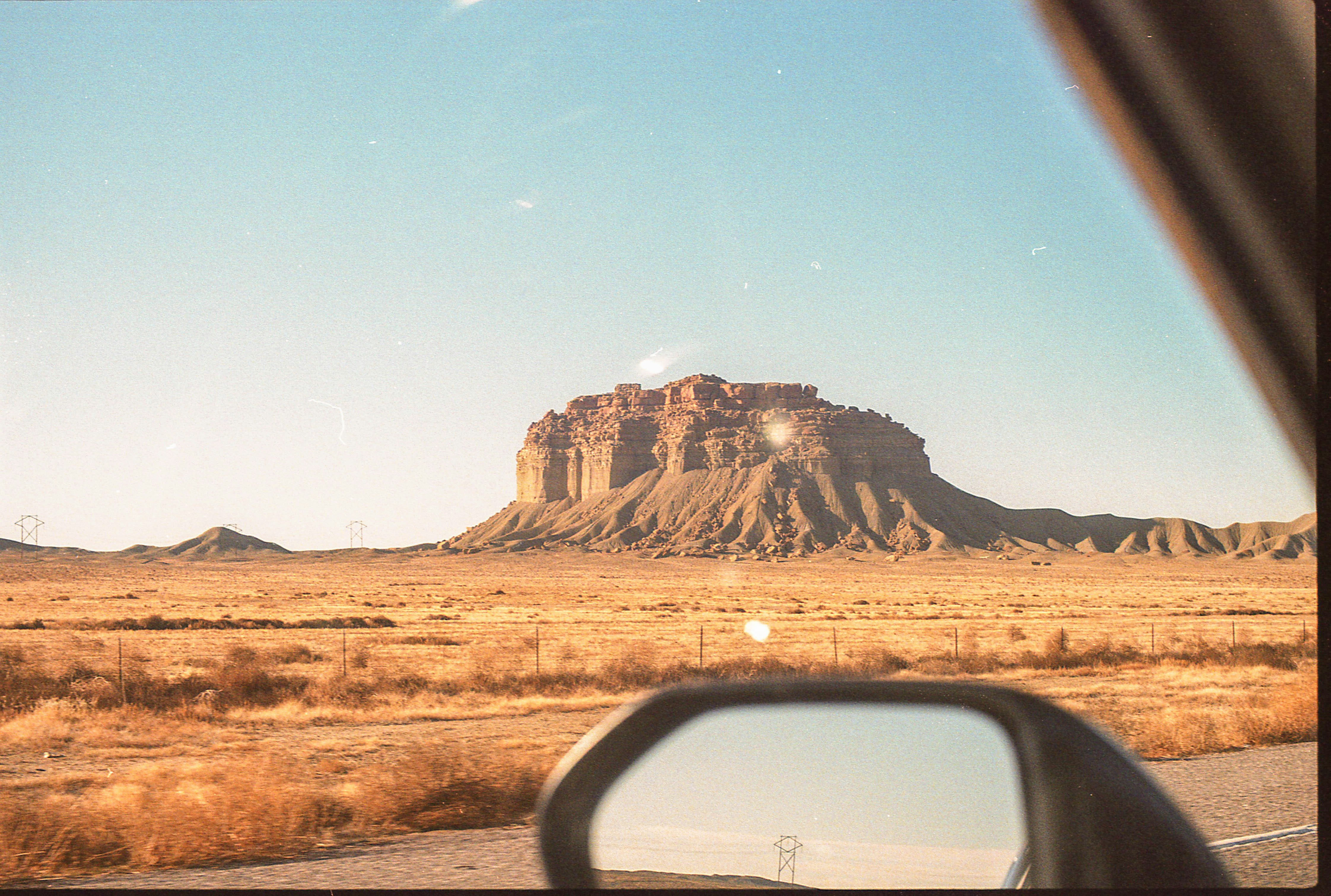 A view of a red rock butte rising from the desert floor in Monument Valley, seen from a car window and side mirror during a drive across the arid landscape